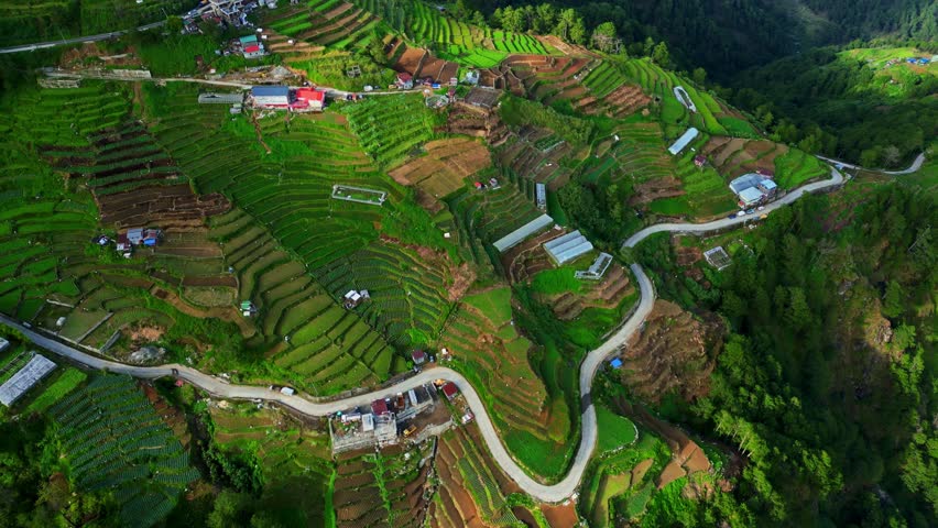 Slow side left aerial over Atok Benguet, Halsema Highway former highest mountain area in the Philippines showing a zigzag highway leading into lush vegetable fields a rural mountain farming.