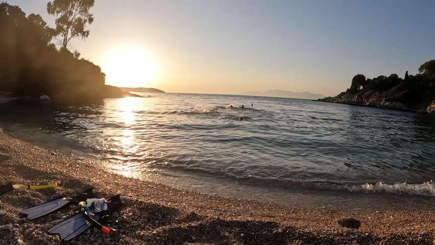 Golden Sunset Over Pebbled Beach with Gentle Waves and Coastal Silhouettes
