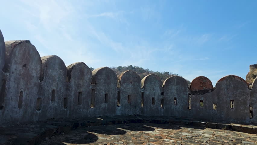 A scenic view of an ancient fort in India, with visitors walking along the pathways surrounded by lush greenery and historical architecture under a clear blue sky.