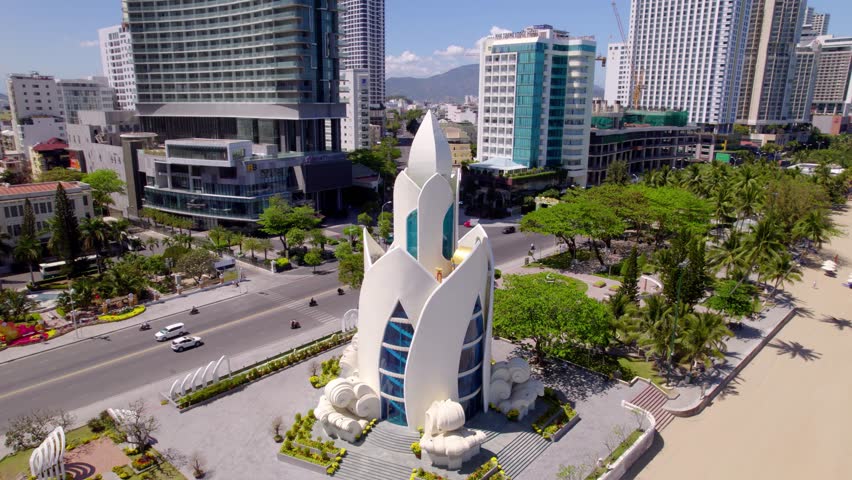 Orbital aerial drone footage circling Tram Huong Tower(Agarwood Tower), a prominent, lotus-shaped landmark on Tran Phu Beach in Nha Trang, Vietnam, symbolizing its coastal charm.