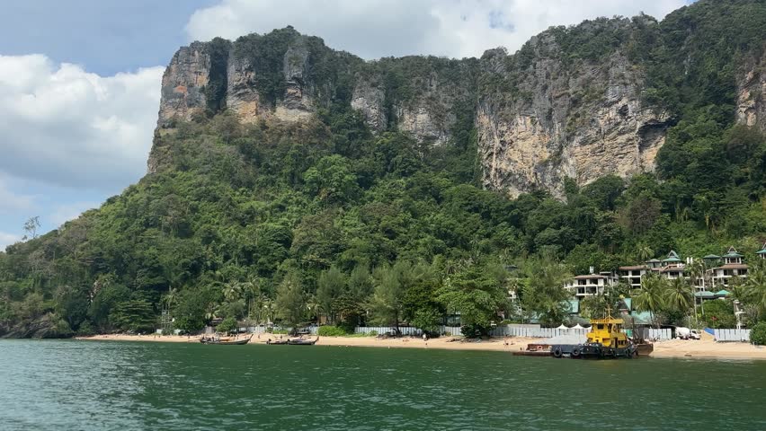 Coastal view at Phra Nang Beach in Krabi Thailand showing sandy shoreline, turquoise water, and dramatic limestone cliffs with greenery along tropical coast