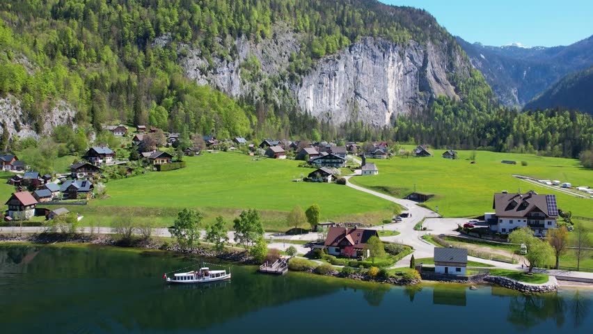 Experience the breathtaking aerial views of Grundlsee Lake in Austria, highlighting the serene waters, green landscapes, and majestic mountains during a clear day.