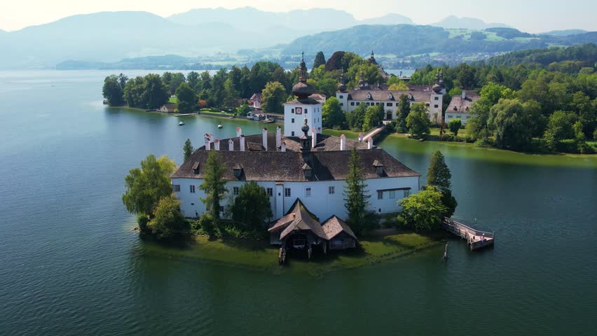 Aerial of beautiful white castle Ort Seeschloss in the Lake Traunsee, at Gmunden town. Serene lake, vibrant boats, and picturesque buildings along the shoreline. Austria tourism and scenic places