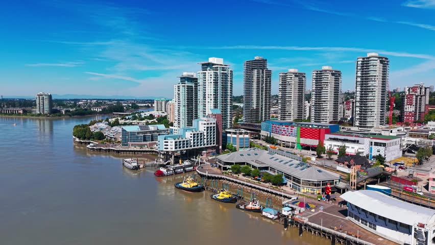 Aerial drone footage of New Westminster skyline along the Fraser River, featuring waterfront buildings, boats, and a clear blue sky in British Columbia.