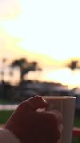 Close up of a female hand holding a white mug of hot coffee or tea with steam rising, enjoying a peaceful morning sunrise from a balcony with a beautiful, soft focus background - Powered by Shutterstock - Get 15% off with code: PIKWIZARD15