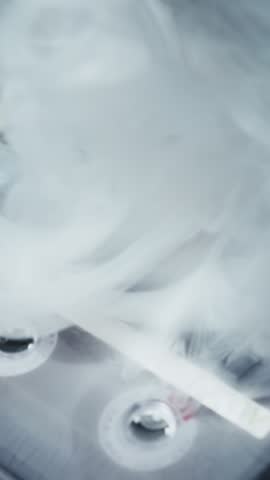 Vintage audio cassette tapes lie stacked on a dark surface. Mysterious white smoke slowly clears, revealing the retro technology in a moody, cool-toned setting.