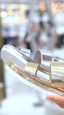 Female hands compare shiny metallic gold and silver sandals while shopping for stylish summer footwear in a bright boutique, deciding between two glamorous seasonal pairs