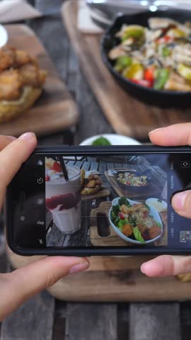 Close up of a food blogger's hands holding a smartphone, capturing images of a delicious lunch spread on a rustic wooden table for social media content, focusing on a healthy salad