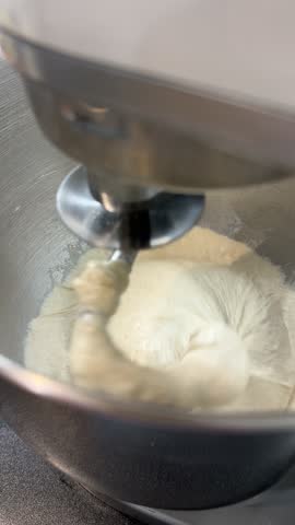 A planetary mixer kneads wheat dough for bread in the kitchen. A close-up of a mixer hook rotating with flour and water. Homemade baking, yeast dough for pizza, sourdoughs.