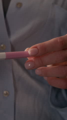 Vertical shot of unrecognizable young girl holding positive pregnancy test with two stripes and showing it to camera