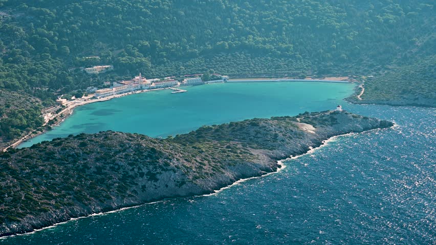 Distant view of Panormitis monastery on Symi island, Greece, set along the coastline with surrounding hills, open sea, and clear sky reflecting the Mediterranean character of the Dodecanese in the Aegean.
