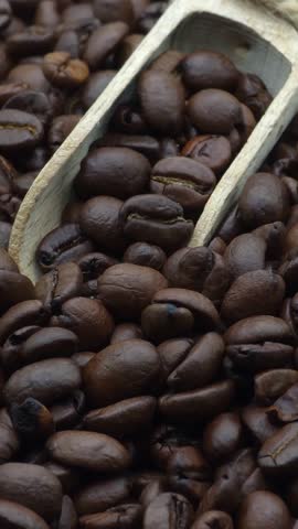 Macro shot of aromatic dark roasted coffee beans with wooden scoop, high-quality cinematic 4K food background for cafe branding, vertical video