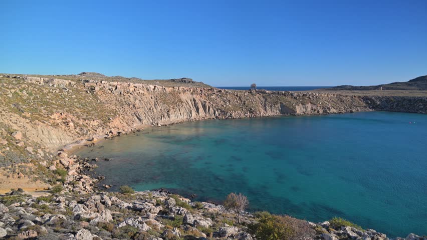 View of a rocky coastal bay with steep limestone cliffs and clear turquoise water near the town of Lindos on the island of Rhodes in Greece