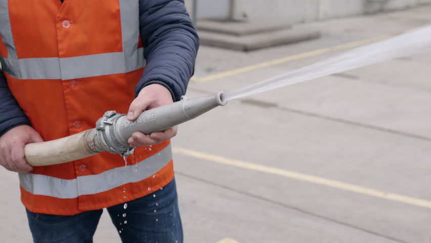 Industrial cleaning, Pressure washing, Water spray. Close-up worker in safety gear operating pressurized water hose, likely for cleaning or industrial maintenance purposes.