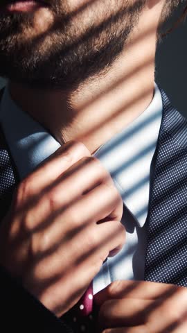 A man adjusts his tie while light casts shadows across his suit in a candid moment.