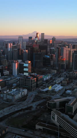Cinematic aerial of Seattle Washington downtown skyline with snowy Mount Rainier on a background and layered city blocks, captured during golden hour showing scale, depth and modern urban structure.