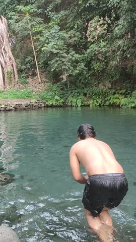 Young man jumping and diving into a clear natural spring pool in a tropical forest, summer vacation adventure, refreshing outdoor swimming activity