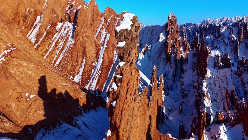 Dramatic snow-capped mountain peaks with striking red rock formations and deep shadows under clear blue sky