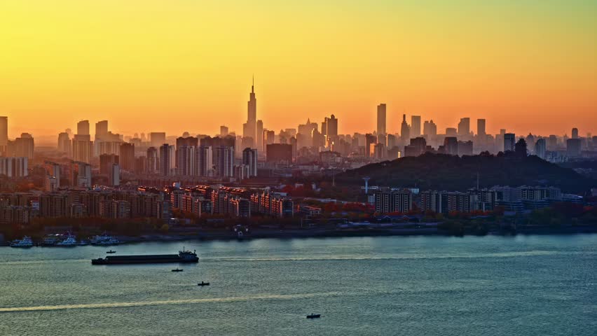 New York City skyline at golden hour sunset with Empire State Building, Hudson River, and cargo ships in foreground during dusk.