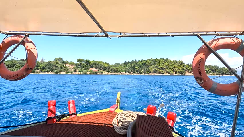 A scenic view from a boat cruising toward a lush tropical island, with vivid blue water, clear skies, and bright sunlight capturing the essence of summer travel.