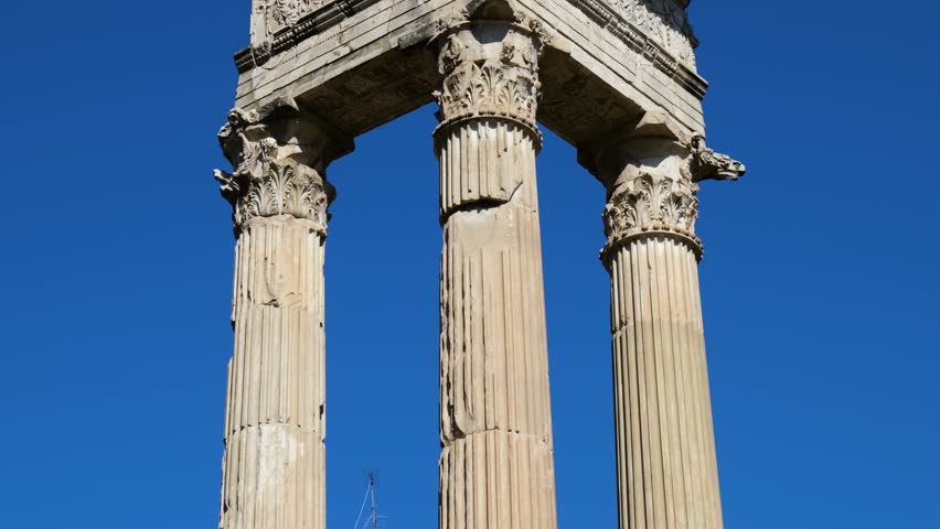 three ancient corinthian columns crowned by elaborately carved entablature floral motifs sculpted figures against vivid blue sky rome up close empire close-up elaborate