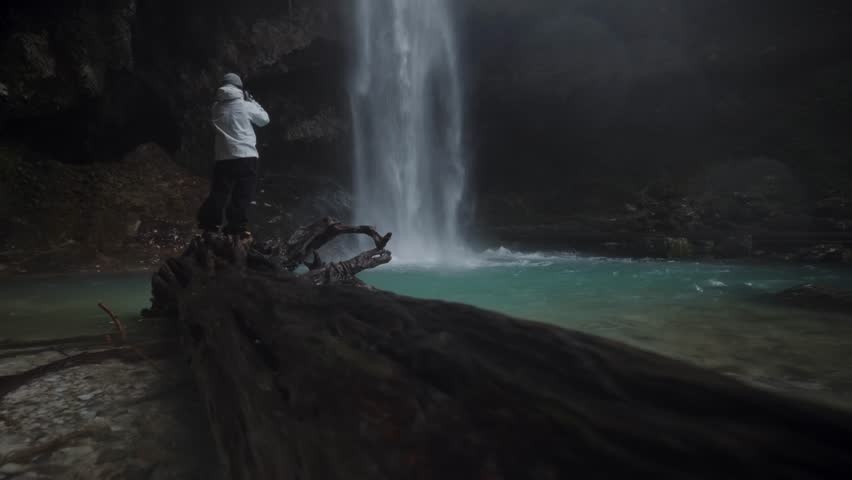 A man in a jacket and trousers on the background of a large waterfall. High quality 4k footage