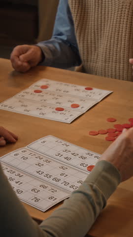 Vertical high angle shot of unrecognizable seniors enjoying bingo at wooden table inside retirement home