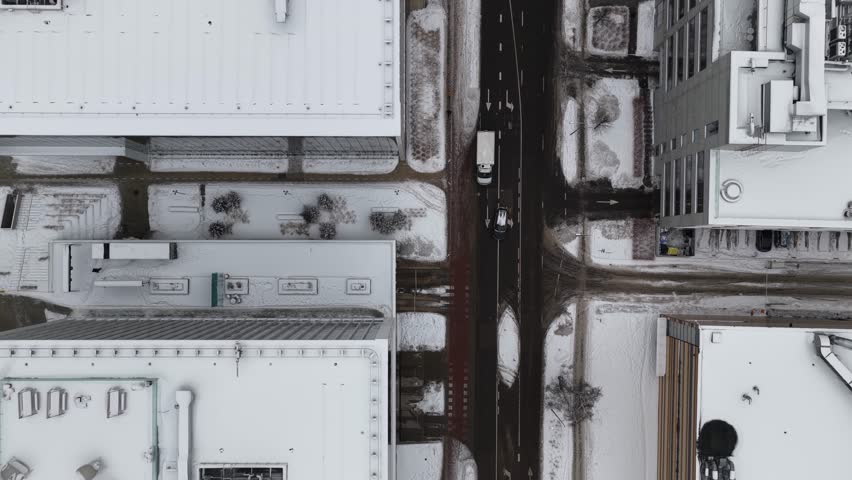 Aerial drone image of a snow-covered city block in Vilnius, Lithuania, showing office buildings, pedestrians, parked vehicles, and an urban street intersection in winter.
