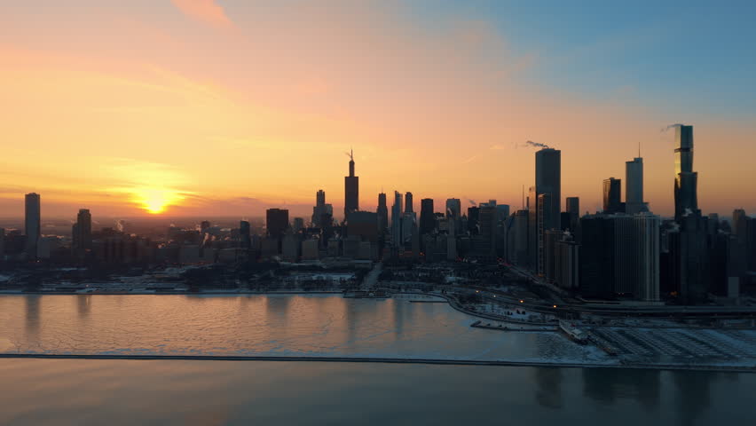 Drone view of downtown Chicago skyline at sunset during winter. The surface of Lake Michigan as subzero temperatures create frozen patterns along the shoreline