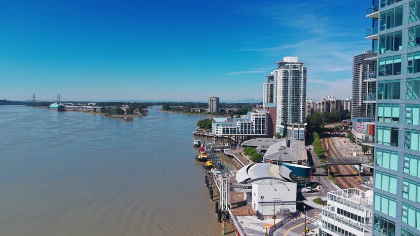 Aerial drone view of The Quay in New Westminster along the Fraser River, featuring waterfront buildings, high-rise towers, and urban riverfront scenery.