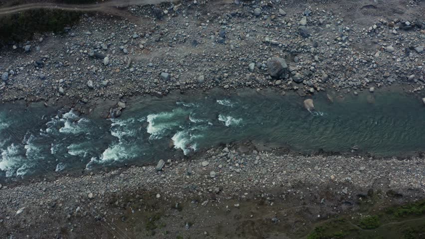 Top-down aerial reveals turquoise Kali River rapids surging through extensive rocky riverbed with grey pebble banks in Pithoragarh Himalayan valley in Uttarakhand, India.