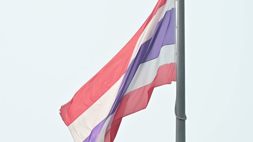 Close up of a Thailand national flag blowing by wind against the sky. The Thai flag, known as the "Tri-Rong" or tricolor.