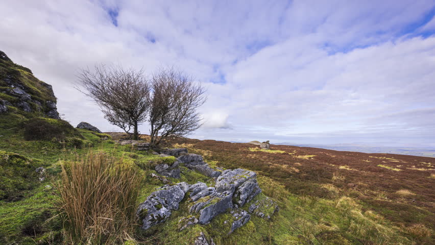 Timelapse of rural landscape with trees and rocks in the foreground grass bogland and hills in distance during cloudy sunny day viewed from Carrowkeel in county Sligo in Ireland.