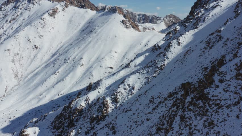 A cinematic drone rising shot over the frozen high-altitude desert of Ladakh, India, revealing a breathtaking panorama of snow-clad mountain ranges under a clear winter sky.