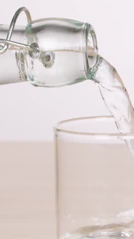 Clear water pours from a glass bottle into a single glass on a table.