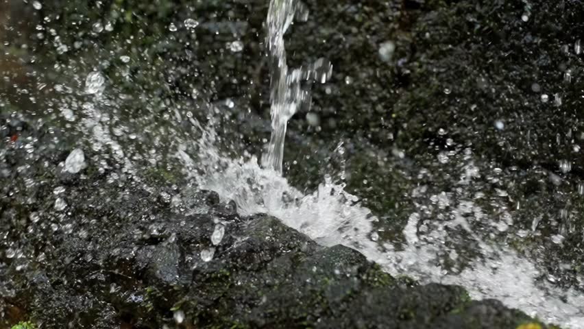 Slow motion close up shot of a water stream falling directly over rocks