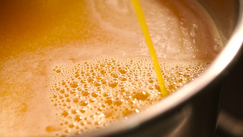 Industrial process of pouring orange juice concentrate into a stainless steel tank. Manufacturing of sweet fruit beverages at a food factory.