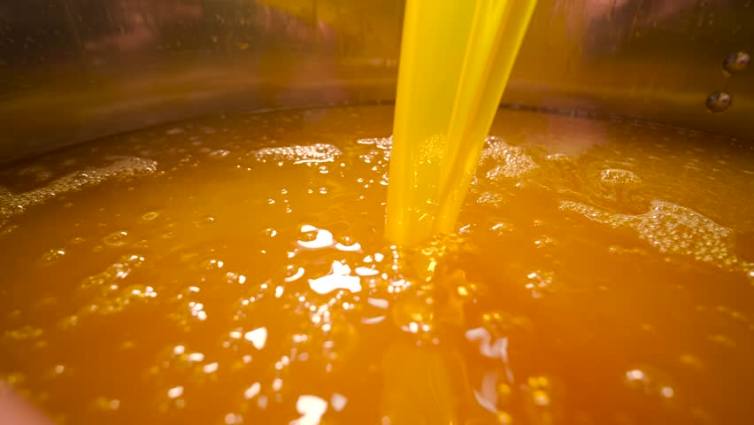 Industrial process of pouring orange juice concentrate into a stainless steel tank. Manufacturing of sweet fruit beverages at a food factory.
