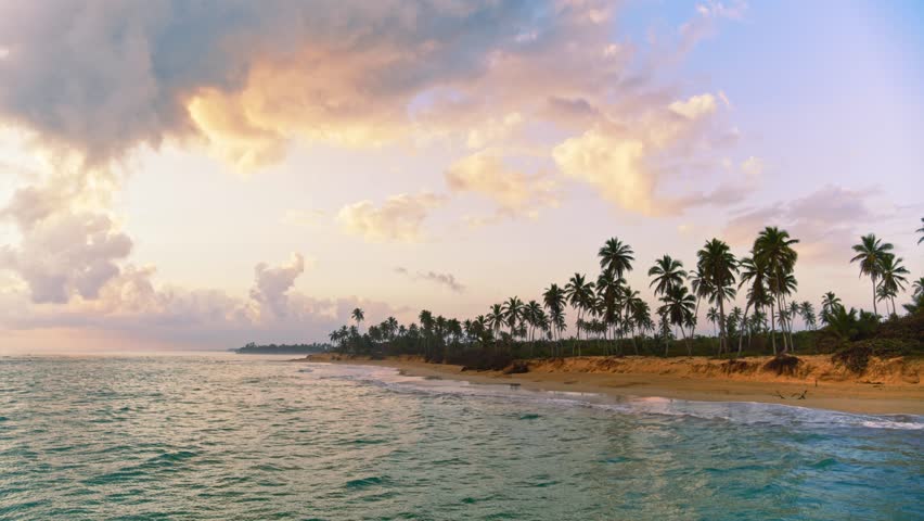 A stunning sunrise sky with clouds over a sandy beach with palm trees. A gentle pink glow over the ocean. Evening sky for meditation. Calm seascape. Horizon over water. Breathtaking sunset over the sea.