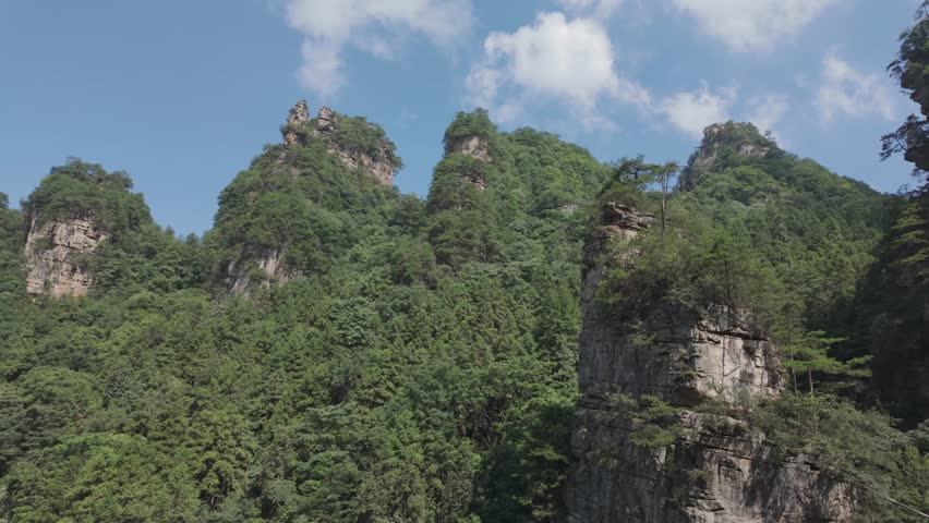 A scenic view of towering green mountains under a clear blue sky. The landscape is rich dense foliage and rugged rock formations. Smooth panning camera movement