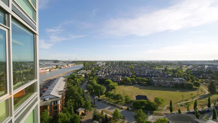 High-rise balcony view overlooking the Fraser River, residential neighborhoods, and green spaces in New Westminster, British Columbia on a bright day.