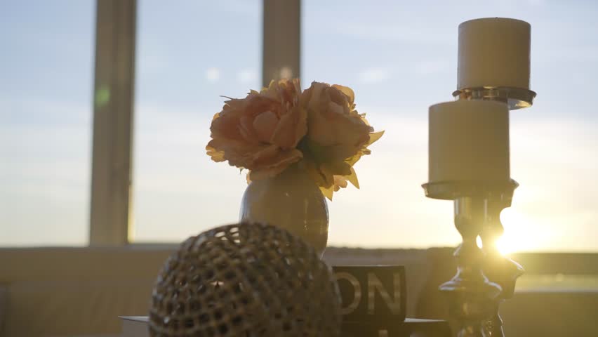 Close-up of elegant home decor with flowers and candles illuminated by soft natural light, creating a calm and inviting interior atmosphere.