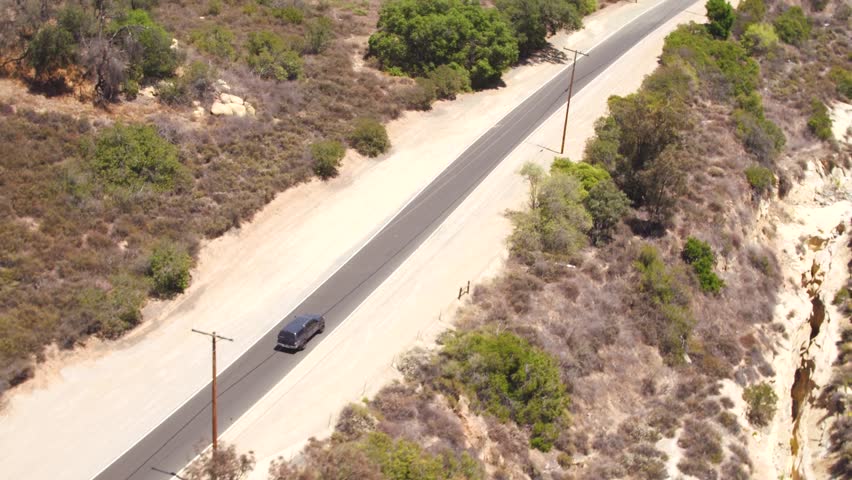 SUV aerial tracking driving down secluded single lane road.