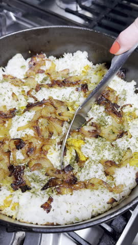 Vertical video - Closeup of a woman’s hand dishing up the first spoons of steaming hot mixed vegetable biryani and basmati rice from a cooking pot into an eating bowl.