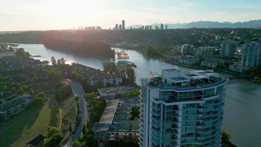 Aerial view of New Westminster at golden hour, featuring a riverside high-rise, Fraser River curves, green neighborhoods, and distant skyline.