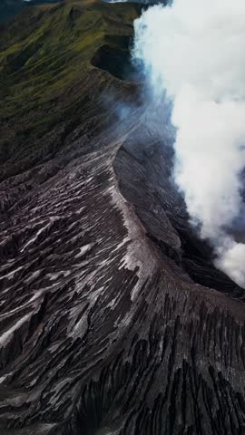 Vertical video of Mount Bromo active volcano in East Java showing volcanic smoke rising along a sharp ridge line with rugged terrain, crater slopes, and dramatic mountain landscape.