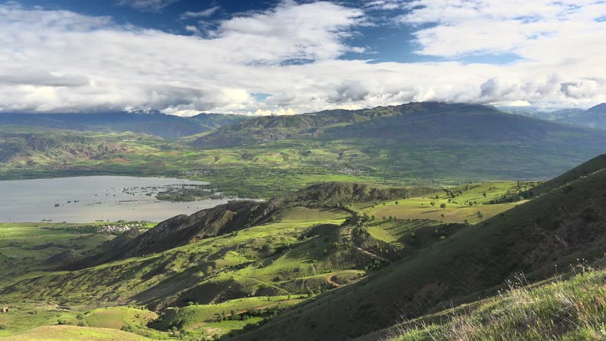 Panoramic lake landscape with green meadows and cultivated fields across rural Venezuela. Fertile plains, pasture, and calm water define an open agricultural basin under cloudy skies.