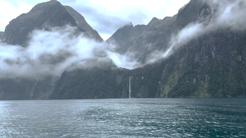 Waterfall and dramatic mountains in Milford Sound fjord, New Zealand travel destination.