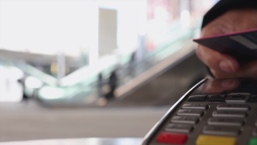 Customer's hand holding a credit card over a pos terminal to complete a purchase transaction
