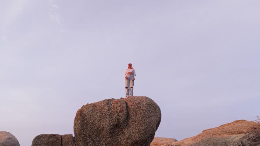 Aerial view of a woman standing on a rock formation in Cape Town, South Africa, during a serene late afternoon
